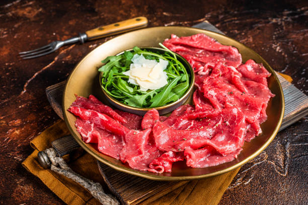 istock Carpaccio Beef meat appetizer with parmesan and arugula. Dark background. Top view 1461427320