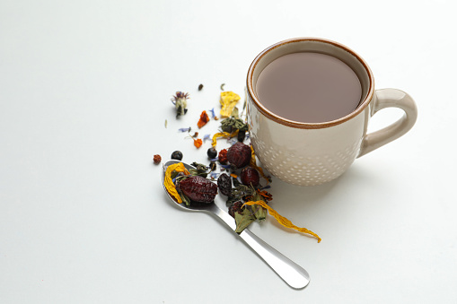 Cup of freshly brewed tea, dried herbs and spoon on white background