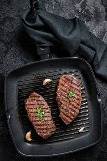 istock Grilled Top Blade or flat iron roast beef meat steaks on a skillet. Black background. Top View 1461429267