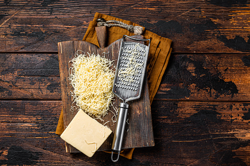 Piece of semi hard cheese and grated cheese with grater. Wooden background. Top view.