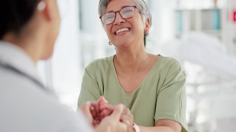 Doctor, elderly patient and holding hands for support at meeting for medical consultation, health advice and healthcare consulting. Doctor appointment, woman listening  and talking to nurse in clinic