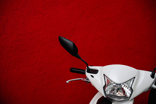 Detail on a modern scooter front side, against a red wall with copy space.
