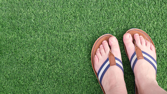 Female legs in flat leather sandals on a green artificial turf. The concept of summer holidays, vacations. Blank for design, space for text, banner.