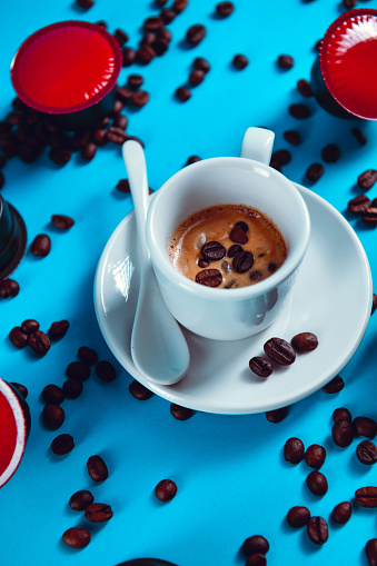 Coffee Beans Spread Around A Cup Of Well Made Espresso On Blue Background
