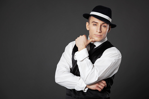 Confident young man posing in gangster style suite. Studio isolated on gray background.