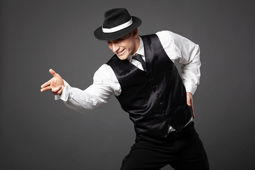 Confident young man dancing in gangster style suite. Studio shot isolated on gray background.