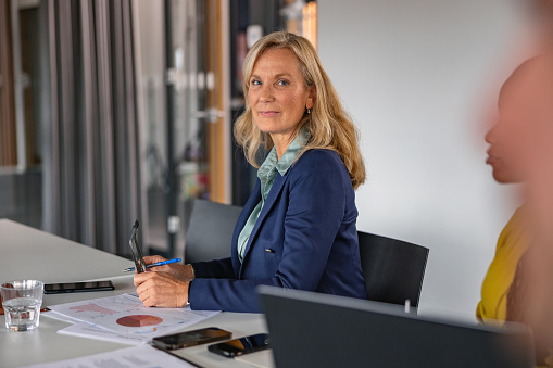 Mature Caucasian businesswoman sitting at a desk in the office attending a business meeting. Looking at camera.