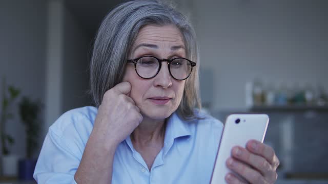 Mature woman in eyeglasses reading sms with spam, shocked with information