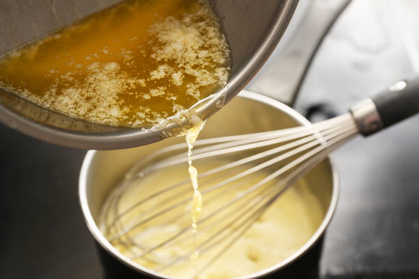 processo de cozimento do molho holandês, despejando manteiga derretida na panela com mistura de ovos, batendo o tempo todo a baixa temperatura para obter uma textura cremosa, foco selecionado - hollandaise sauce fotos - fotografias e filmes do acervo