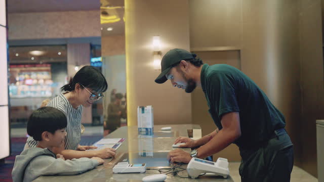 Asian single mother with son in front cinema ticket counter checking movie show time buying movie ticket.