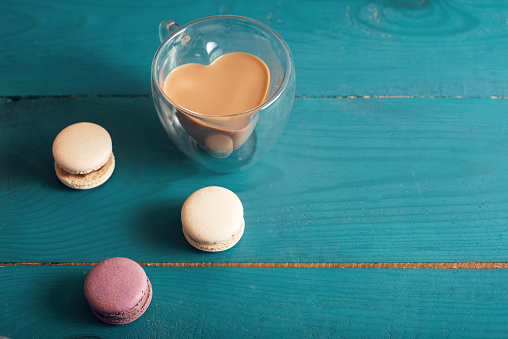 Tasty almond macarons and heart shaped cup of coffee with milk on the blue wood surface. Vintage, romantic style. Top view