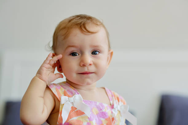 Portrait of little blond girl touching her ear and looking at camera