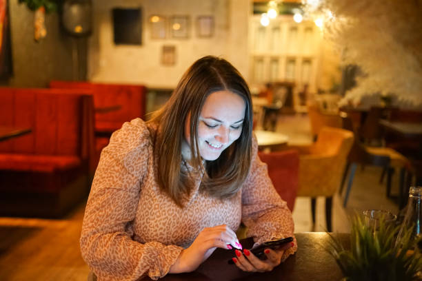 istock Smiling young woman siting in restaurant while texting on her mobile phone. 1461453894