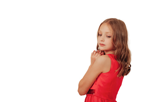 Pensive stylish little girl model in pink dress posing at isolated empty white background, looking down. Adorable girl shooting posing in studio. Modelling concept. Copy text space for advertising