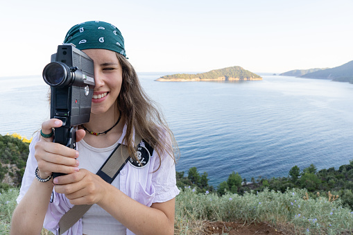 A teen girl is filming with a retro camera on her vacation