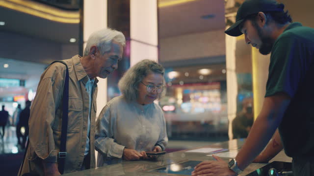 Asian senior couple choosing a movie and buying movie tickets at the ticket counter.