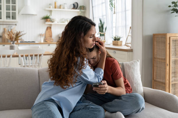 Caring kind woman hugging upset crying teen girl sits on sofa with phone and suffering from stress Upset crying teenage girl sits on sofa with phone suffering from depression after bullying. Caring kind woman hugging daughter feeling stressed because of insults in social networks or messengers woman comforting depressed friend stock pictures, royalty-free photos & images