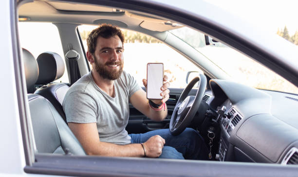 istock young man smiling showing the screen his phone, sitting on driver's seat, app driver calling user 1461463037