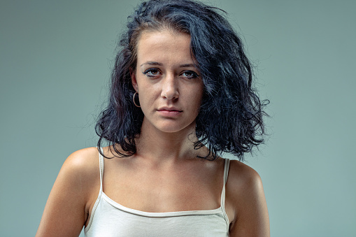 Frontal portrait of serious girl. Determined or about to get angry? She has black hair and a white tank top. Perhaps she is simply expressionless and there is no reason for it.