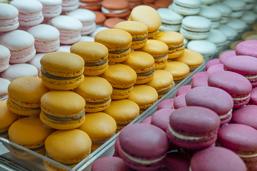 Variety of macarons or macaroons displayed in a coffee shop window, French desert stacked by color and flavors, popular sweet meringue-based cookie with a light airy consistency and crunchy texture.