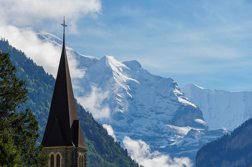Swiss alpine forest and snow-covered peaks behind a church steeple