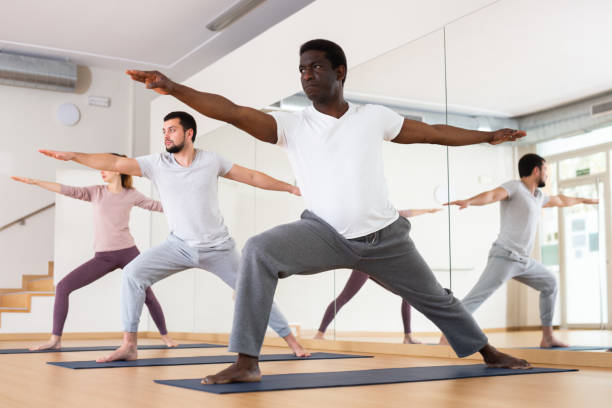 afro-americano em pé em virabhadrasana durante treinamento de power yoga - stretching yoga men good posture - fotografias e filmes do acervo