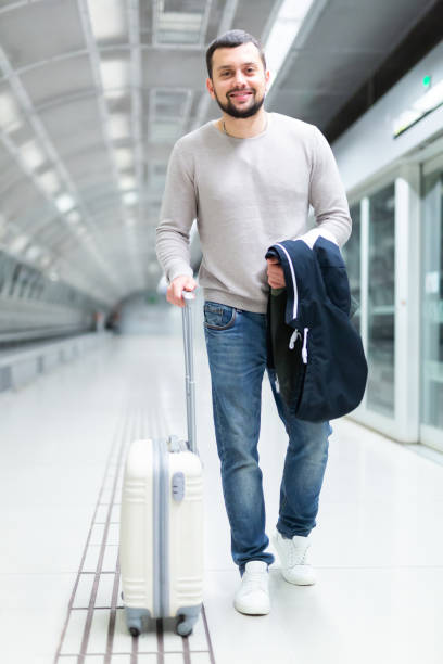 istock Smiling bearded guy walking along platform of subway station with suitcase 1461473321