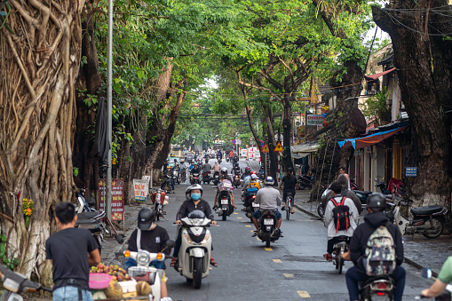 Hoi An, Vietnam - November 23, 2022: Commuters on motor bikes traversing a road in the beautiful and historic Hoi An, a UNESCO World Heritage Site in Vietnam, Southeast Asia.