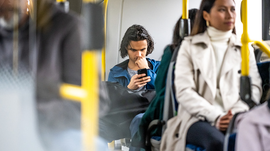 Young man reading from smartphone in city bus. Male passenger sitting in public transport and using mobile phone, medium shot