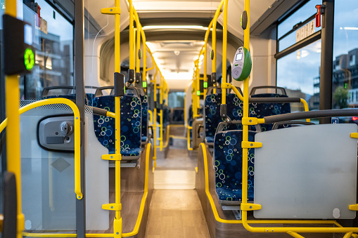 Modern empty commuter bus aisle interior with nobody inside. Seats and yellow metal handrails in passenger public transport