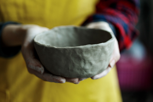 Woman potter's hands holding handmade unbaked ceramic bowl
