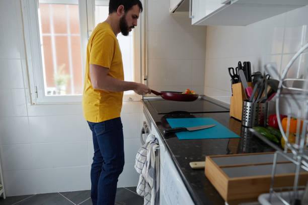 istock Side view of a bearded young man moving a frying pan while cooking in an illuminated kitchen 1461486458