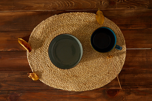 Wicker placemat under small plates. Autumn leaves on wooden background.