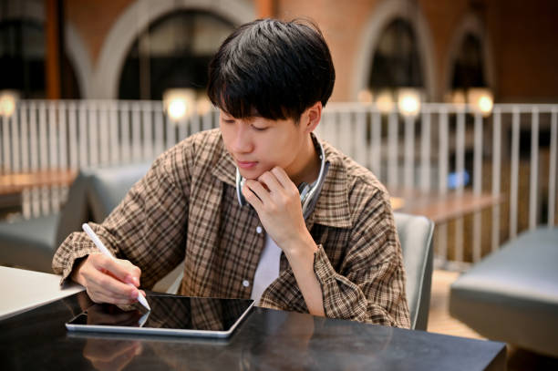 istock Handsome and focused young Asian man taking notes on a digital tablet, remote working at cafe. 1461496832