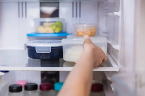 Photo of Asian woman stored leftovers food in plastic container put into refrigerator.