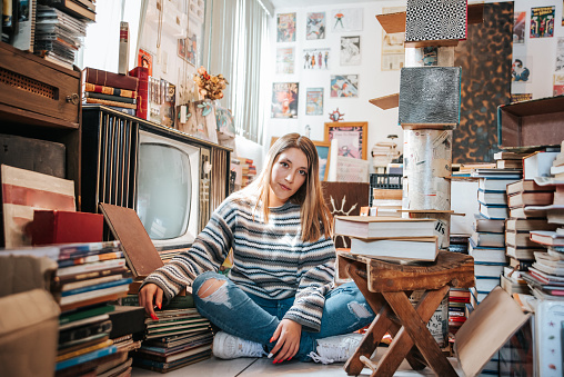 Portrait of young woman in a bookstore posing in a vintage style, wearing a sweatshirt.