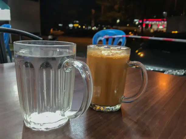 Photo of Selective focus with noise effect of glass with fresh water and tea with milk or popularly known as Teh Tarik