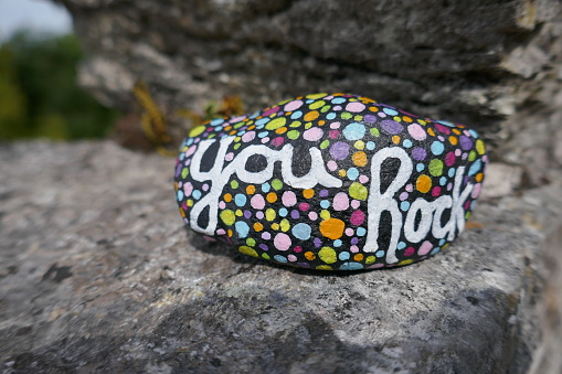 Encouraging and uplifting message painted on kindness rock on top of larger rock