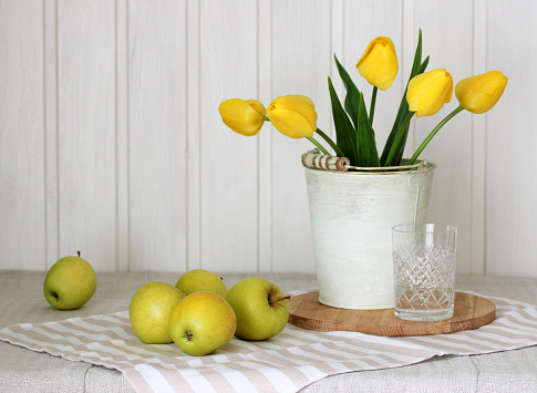 spring still life with yellow apples and yellow tulips on the table in the cottage. flowers and fruits.