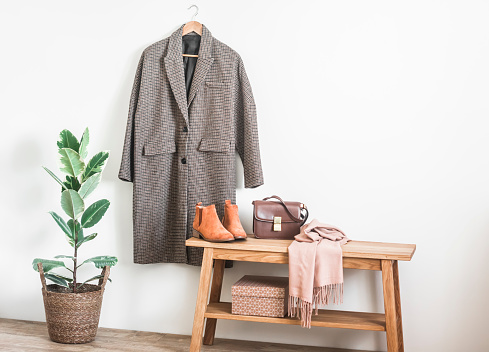 An English style coat on a hanger, a bench with a bag, a homemade flower in a basket in the hallway