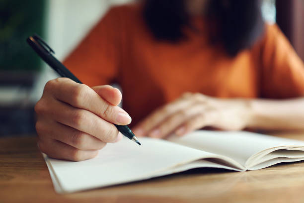 primo piano della donna che scrive a mano sul taccuino. - scrivere foto e immagini stock