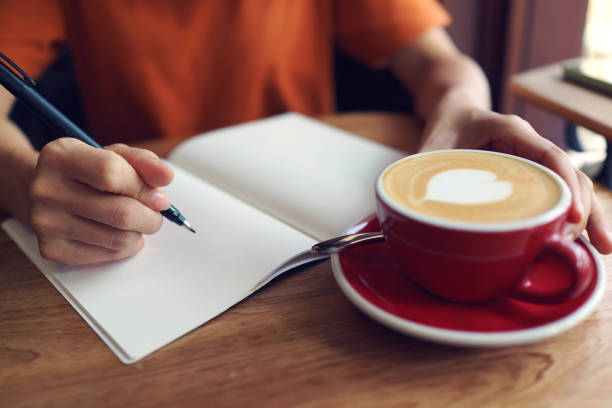 istock Hand holding pen, writing on a notebook, coffee cup on wooden desk. 1461537141