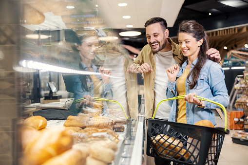 Smiling couple is buying and choosing pastry at bakery department at marketplace.