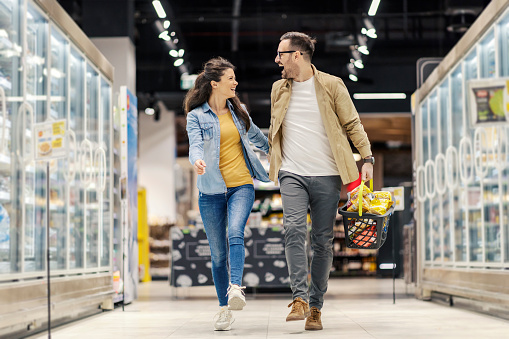 An overjoyed couple is skipping and holding hands in supermarket during shopping.