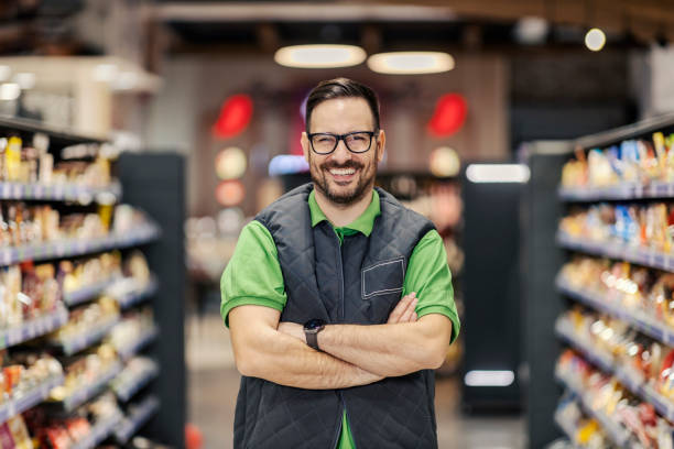 A successful seller is standing at supermarket with arms crossed and smiling at the camera. stock photo