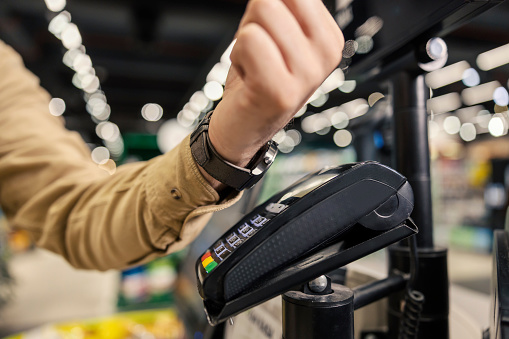 Male's hand paying with smart watch at hypermarket at self-service checkout.