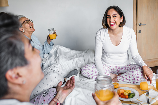 Hispanic happy family of women, grandmother, daughter having breakfast in bed at home in Mexico Latin America