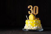The number Thirty on a yellow cake for an anniversary or birthday in a dark key.