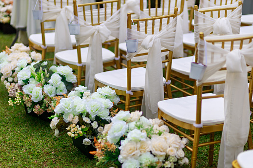 Chairs for a wedding reception decorated with fabric or a veil. Outdoor wedding ceremony decorated with bouquets of flowers.