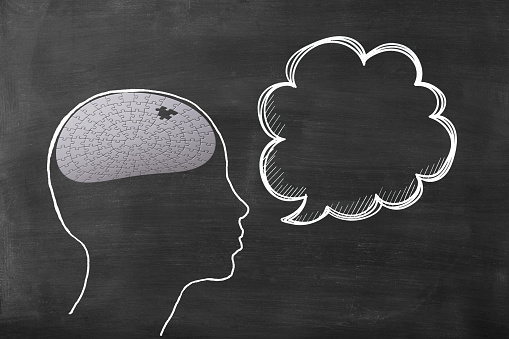 Chalk drawn human head shape with jigsaw puzzle, and blank speech bubble on blackboard with copy space.